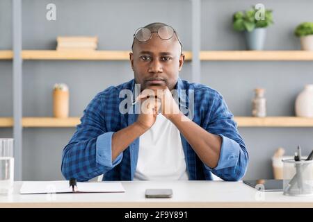 Portrait of serious african american businessman looking at camera while sitting at home at workplace Stock Photo