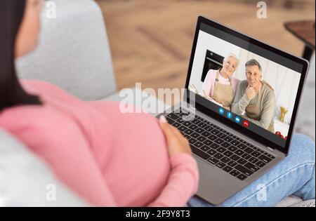 Unrecognizable Pregnant Woman Using Laptop At Home, Video Chatting With Senior Parents Stock Photo