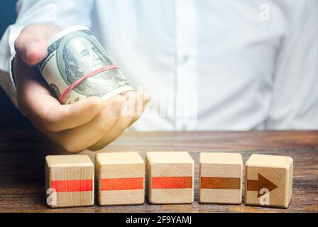 Man holds money above of blocks of red arrow. Financing and investing in completion of a business project. Bribes in exchange for stopping slowdown of Stock Photo