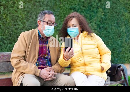 Caucasian elderly couple using a mobile phone. They are outdoors and wearing face masks. Stock Photo