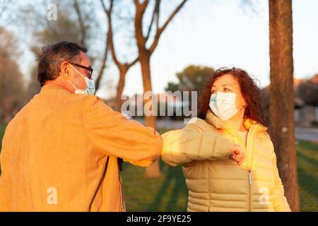 Two older people wearing face masks greet each other with elbows together. Concept of social distancing and new normal. Stock Photo
