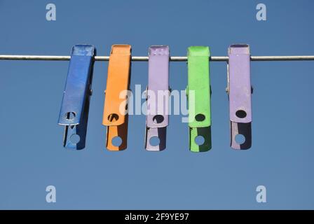 Front view of colorful cloth clips hanging on wire with blue sky in background Stock Photo