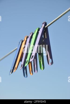 Low angle shot of multicolored cloth pins hanging on wire in outdoor with blue sky in background Stock Photo