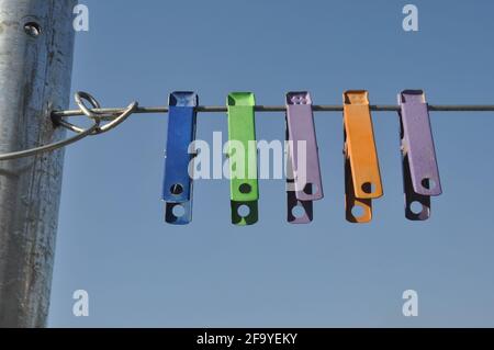 Front view of colorful cloth clips hanging on wire with blue sky in background Stock Photo