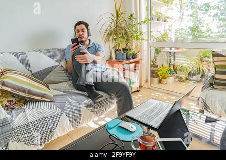 Young Jewish man wearing headphones and sitting on his couch at home Stock Photo