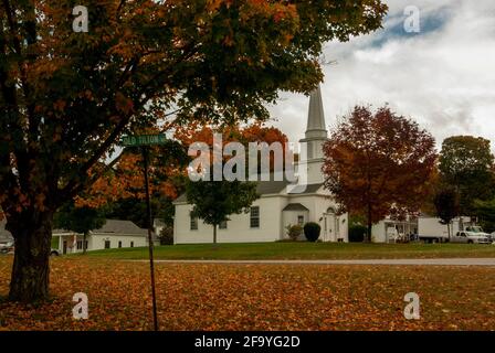 The white, wooden Canterbury United Community Church, New Hampshire, USA amongst  fallen leaves and red foliage in autumn / fall Stock Photo
