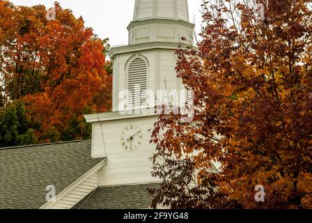 The white, wooden clock tower of Canterbury United Community Church, New Hampshire, USA amongst red foliage in autumn / fall Stock Photo
