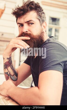 Guy having rest at cafe terrace. Hipster, client, visitor on thoughtful face sits at cafe outdoor. Man with beard and mustache in calm mood while Stock Photo