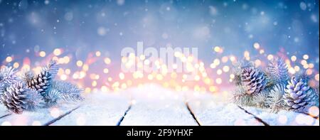 Fir Branches And Pinecones On Snowy Table And Christmas Lights Stock Photo