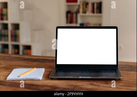 Front view at a laptop screen with an empty white screen for your presentation stands on a wooden table, notebook lies nearby. Mockup, copy space concept Stock Photo