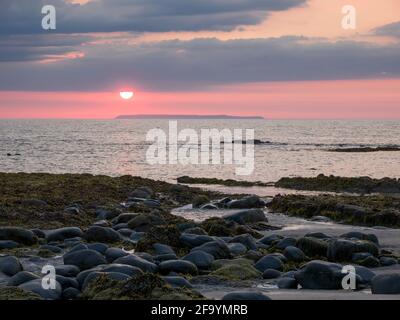 The setting sun over Lundy Island with Peppercombe beach in the foreground, North Devon, England. Stock Photo