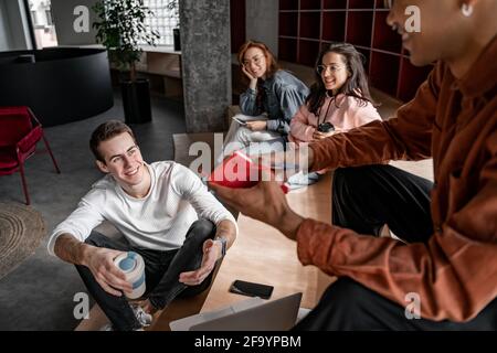 blurred african american student holding notebook near happy classmates sitting on stairs Stock Photo