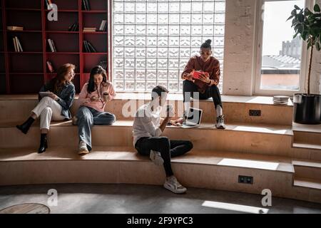interracial students sitting on stairs and using gadgets Stock Photo