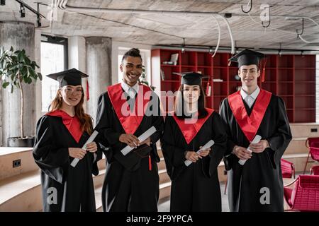 happy interracial students in graduation gowns and caps holding diploma, senior 2021 Stock Photo