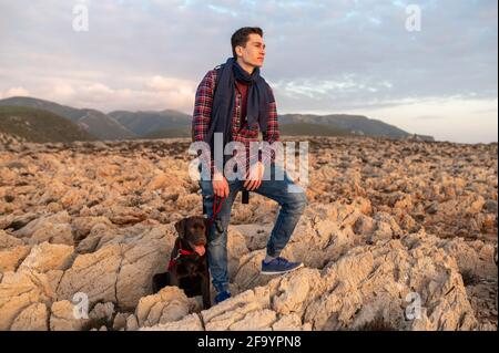 Young handsome hiker man in a remote location standing looking away next to his dog. Stock Photo