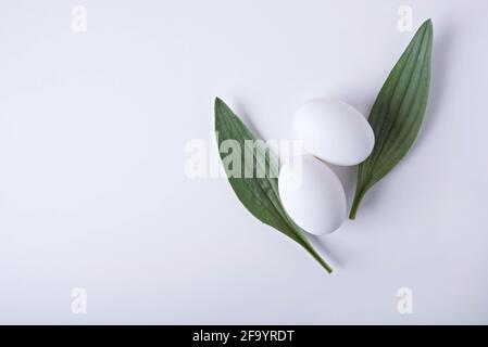 Minimalistic Easter composition. Two eggs and two leaves similar to rabbit ears on a white background. Stock Photo