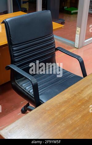 The black leather armchair near the old wooden table in the local office, soft and comfortable for work all day, front view for the copy space. Stock Photo