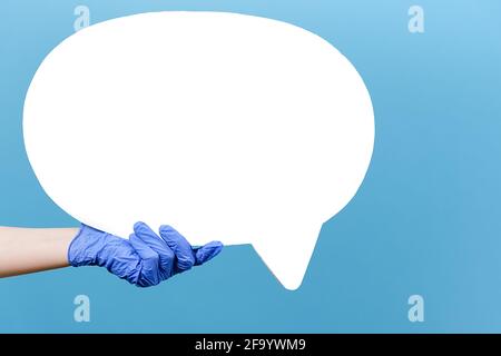 Close up of unrecognizable male in medical gloves hold white paper blank speech bubble, isolated over blue studio background with copy space Stock Photo