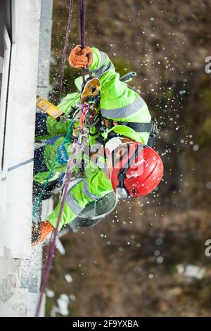 Industrial climber during winterization works, cutting styrofoam boards and styrofoam dust falling down Stock Photo