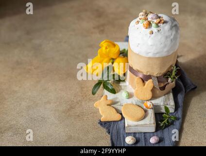 Easter composition with traditional Orthodox sweet bread. Kulich decorated with meringue icing, candy shaped eggs, easter cookies and tulip. Selective Stock Photo