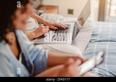 Close up of female hands typing on laptop keyboard at home near his unrecognizable girlfriend. Business, working from home, studying online concept. Stock Photo