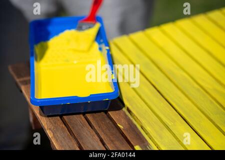 Closeup shot of yellow paint and a brush on a half-painted wooden table Stock Photo