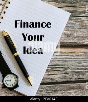 Top view of a pen and a watch with Finance Your Idea written on a notebook. Stock Photo