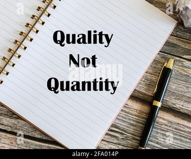 Top view of a pen with Quality Not Quantity written on a notebook. Stock Photo