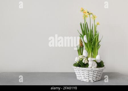 Easter flowers composition with blossom narcissus, hyacinth and organic eggs in white wicker basket. Spring flowering bulbs in a potting. Copy space. Stock Photo