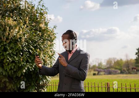 African American businessman elegantly dressed makes a video call with his colleague using wireless headphones Stock Photo