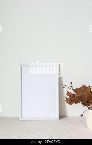 Home decor mocap, empty picture frame near white painted concrete wall, branches with dry leaves Stock Photo