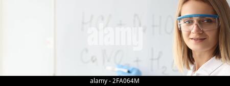 Woman scientist in protective gloves showing chemical formulas on blackboard Stock Photo