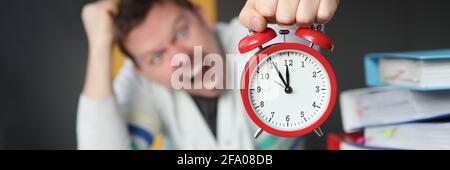 Man shouting and holding red alarm clock at table in office closeup Stock Photo