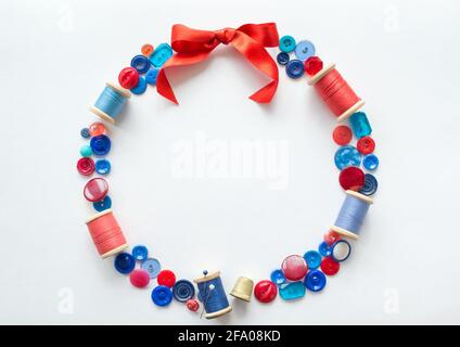 Wreath is made of buttons and threads of red and blue colors with pins and a bright bow of satin ribbon at the top. Copy space. Stock Photo