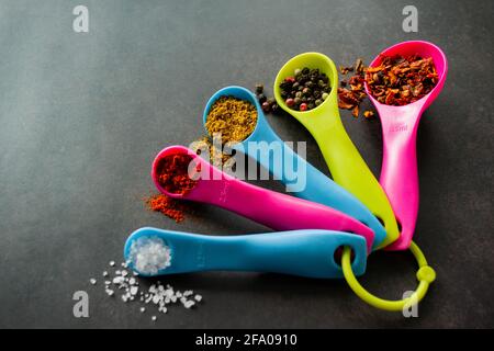 Closeup multicolored measuring spoons with spices: chili flakes, a mix of pepper peas, curry, paprika and coarse sea salt. Black chalk board backgroun Stock Photo