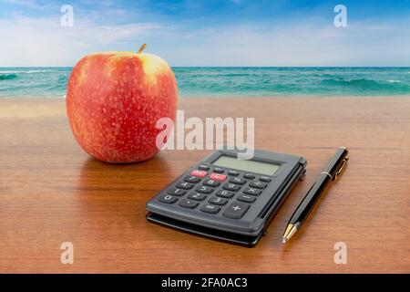 Apple calculator pencil lie on the table against the backdrop of the sea Stock Photo