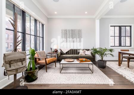 A bright living room with natural light pouring in. A green couch and orange leather chair are surrounding a modern coffee table. Stock Photo