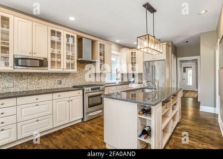 https://l450v.alamy.com/450v/2fa0and/a-luxurious-cream-colored-kitchen-with-black-granite-counter-tops-stainless-steel-kitchenaid-appliances-and-edison-bulbs-above-the-island-2fa0and.jpg