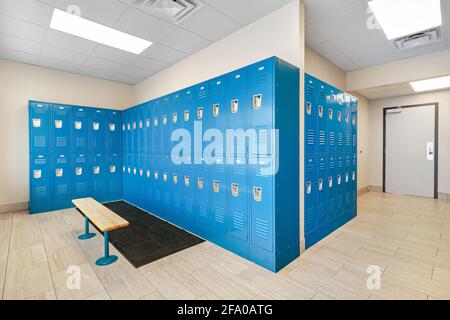 A clean locker room with bright blue lockers and a bench mounted to the floor. Stock Photo