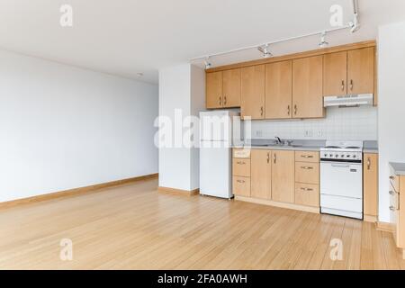 A maple kitchen in an empty city apartment with white appliances, granite countertops, plenty of cabinets for storage, and hardwood floors. Stock Photo