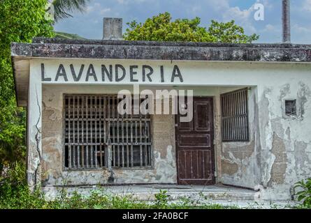 Mexican landromat or Lavanderia in grungy old building with stucco falling off concrete blocks and wooden bars at windows - weeds growing all around a Stock Photo