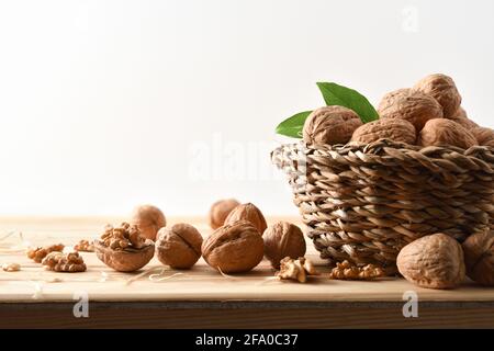 Basket full of walnuts on a wooden table with split walnuts with seeds in sight with white isolated background Stock Photo