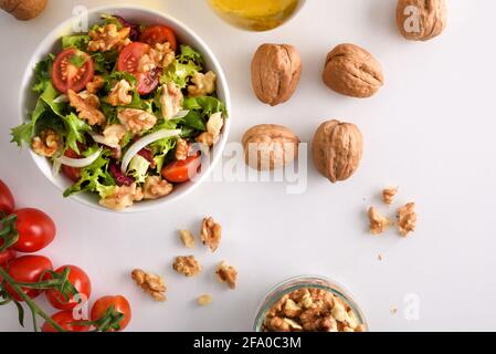 Mediterranean salad with walnuts in a bowl with olive oil and walnuts on a white table. Top view Stock Photo