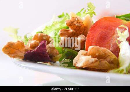 Mediterranean salad with walnuts in a bowl with lettuce tomatoes and onion and olive oil on a white table isolated background. Front view. Stock Photo