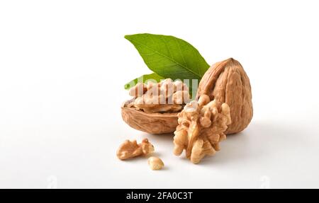 Walnuts in shell and broken showing seeds with leaves on white table and white isolated background. Front view. Stock Photo