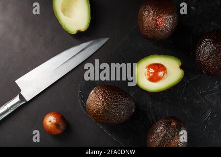 Sliced and whole organic avocado Hass with a knife on a black background. A source of essential fats, vitamins, trace elements, beta-carotene and omeg Stock Photo