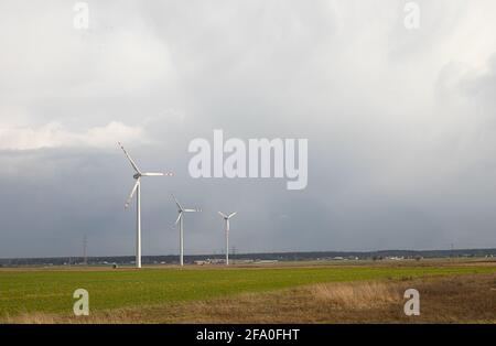 Wind turbines, three modern windmills on a green field before the storm Stock Photo