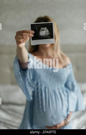 A portrait of a pregnant woman showing an ultrasound picture of her unborn baby into a camera. An expectant woman with a sonogram. Stock Photo