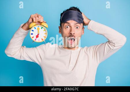 Photo portrait of screaming gasping shocked man touching head holding yellow clock in one hand isolated on vivid blue colored background Stock Photo