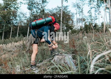 A female backpacker lacing her hiking shoes in the woods. A hiker tying laces of her trekking boots. Stock Photo